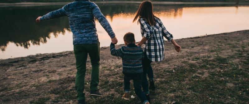 Photo of two adults with a child, walking towards a river and holding hands