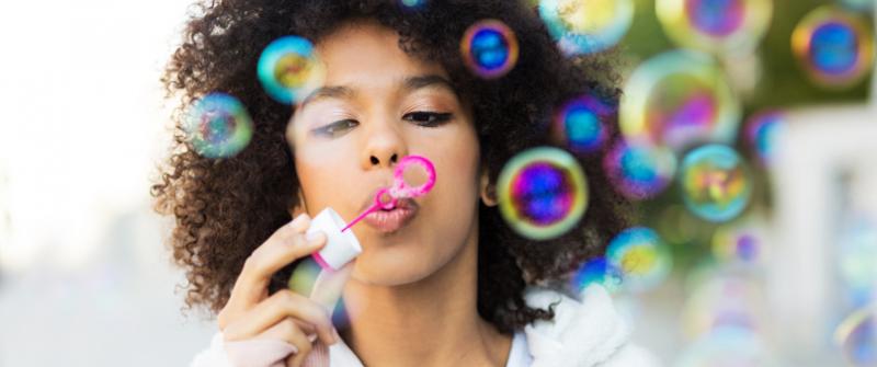 Woman Blowing Bubbles Photo of a woman holding a pink bottle of bubble solution while blowing into a bubble wand. Bubbles are floating off into the air.