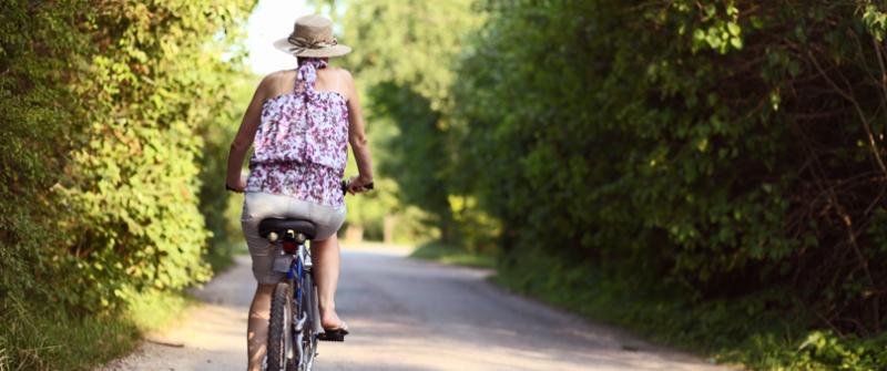 Woman Biking Photo of a woman riding her bike down a paved, tree-lined road.