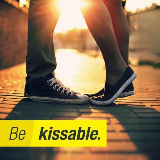 Feet and legs of two people kissing in front of sunset with text stating 'Be kissable'